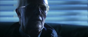 Movie still from “The Hunger” (1983), directed by Tony Scott – An older man wearing glasses and a black shirt; Close Up shot, Low angle