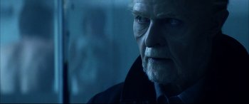 Movie still from “The Hunger” (1983), directed by Tony Scott – An old man with a beard and a goatee looking at the camera; Close Up shot, Over the shoulder angle