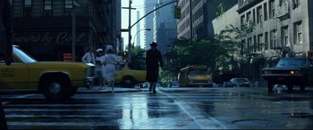 Movie still from “The Hunger” (1983), directed by Tony Scott – A man in a black coat crosses a wet street; Wide shot, Low angle