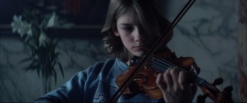 Movie still from “The Hunger” (1983), directed by Tony Scott – A young person playing a violin in a dark room; Close Up shot, Low angle