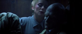 Movie still from “The Hunger” (1983), directed by Tony Scott – A woman standing in front of a man with a face mask on; Close Up shot, Low angle