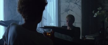 Movie still from “The Hunger” (1983), directed by Tony Scott – A woman sitting in front of a mirror holding a drink; Medium shot, Over the shoulder angle