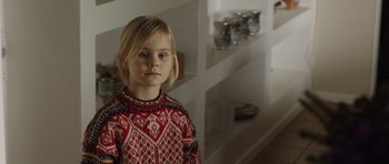 Movie still from “The Hunt” (2012), directed by Thomas Vinterberg – A little girl wearing a red and black sweater; Close Up shot, Over the shoulder angle