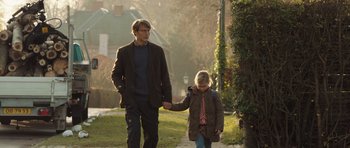 Movie still from “The Hunt” (2012), directed by Thomas Vinterberg – A man and a girl walking down a sidewalk holding hands; Medium shot, Low angle