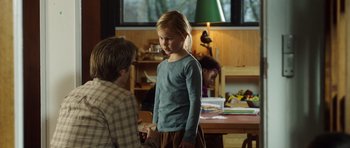 Movie still from “The Hunt” (2012), directed by Thomas Vinterberg – A little girl standing next to a man in a room; Medium shot, Over the shoulder angle