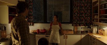Movie still from “The Hunt” (2012), directed by Thomas Vinterberg – A woman in an apron standing in front of a microwave oven; Medium shot, High angle