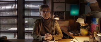 Movie still from “The Hunt” (2012), directed by Thomas Vinterberg – A woman sitting at a table in front of a window; Medium shot, Low angle