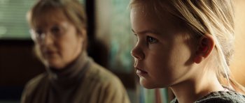 Movie still from “The Hunt” (2012), directed by Thomas Vinterberg – A little girl looking at the camera while sitting next to another girl; Close Up shot, Over the shoulder angle
