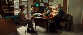 Movie still from “The Hunt” (2012), directed by Thomas Vinterberg – Three people are sitting at a table in an office; Wide shot, Over the shoulder angle