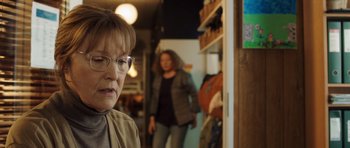 Movie still from “The Hunt” (2012), directed by Thomas Vinterberg – A woman in glasses and a jacket standing next to a woman; Close Up shot, Over the shoulder angle