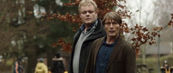 Movie still from “The Hunt” (2012), directed by Thomas Vinterberg – A couple of men standing next to each other in front of a tree; Medium shot, Low angle