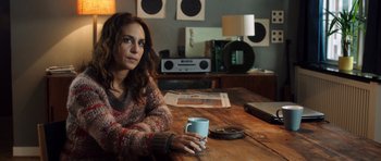 Movie still from “The Hunt” (2012), directed by Thomas Vinterberg – A woman sitting at a wooden table holding a coffee mug; Medium shot, Over the shoulder angle