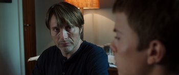 Movie still from “The Hunt” (2012), directed by Thomas Vinterberg – A man sitting in front of another man in front of a lamp; Close Up shot, Over the shoulder angle