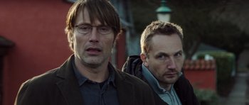 Movie still from “The Hunt” (2012), directed by Thomas Vinterberg – Two men standing next to each other in front of a building; Close Up shot, Low angle