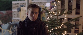 Movie still from “The Hunt” (2012), directed by Thomas Vinterberg – A young man wearing a scarf standing in front of a christmas tree; Close Up shot, Over the shoulder angle