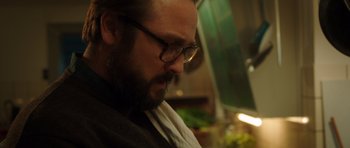 Movie still from “The Hunt” (2012), directed by Thomas Vinterberg – A man with a goatee wearing glasses looking down; Close Up shot, Low angle