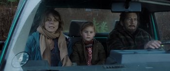 Movie still from “The Hunt” (2012), directed by Thomas Vinterberg – A woman and two children sitting in the back seat of a car; Medium shot, Over the shoulder angle