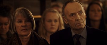 Movie still from “The Hunt” (2012), directed by Thomas Vinterberg – A man and a woman are sitting next to each other in front of another man; Close Up shot, Over the shoulder angle