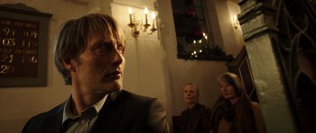 Movie still from “The Hunt” (2012), directed by Thomas Vinterberg – A man and two women are sitting in front of a window; Close Up shot, Low angle