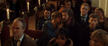 Movie still from “The Hunt” (2012), directed by Thomas Vinterberg – A man and a woman sitting next to each other in front of other people; Close Up shot, Over the shoulder angle