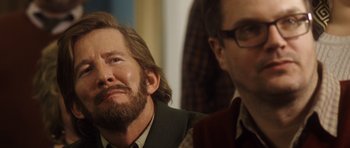 Movie still from “The Hunt” (2012), directed by Thomas Vinterberg – A man with long hair and a goatee is sitting next to another man; Close Up shot, Over the shoulder angle