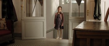 Movie still from “The Hunt” (2012), directed by Thomas Vinterberg – A little girl standing in front of a doorway; Wide shot, High angle