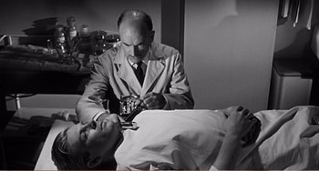 Movie still from “The Incredible Shrinking Man” (1957), directed by Jack Arnold – An old photo of a man getting a tattoo on his arm; Medium shot, Low angle