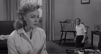 Movie still from “The Incredible Shrinking Man” (1957), directed by Jack Arnold – A woman sitting in front of a chair in a living room; Medium shot, Over the shoulder angle