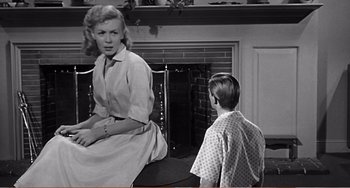 Movie still from “The Incredible Shrinking Man” (1957), directed by Jack Arnold – A woman sitting in front of a boy in front of a fireplace; Medium shot, Over the shoulder angle