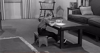Movie still from “The Incredible Shrinking Man” (1957), directed by Jack Arnold – A man sitting at a table writing on a piece of paper; Wide shot, High angle