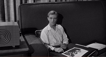 Movie still from “The Incredible Shrinking Man” (1957), directed by Jack Arnold – A black and white photo of a man sitting at a table; Medium shot, High angle