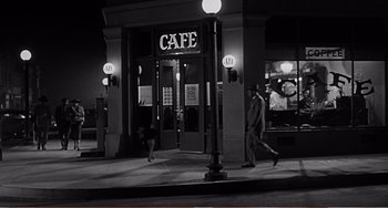 Movie still from “The Incredible Shrinking Man” (1957), directed by Jack Arnold – Two people walking in front of a cafe at night; Wide shot, High angle