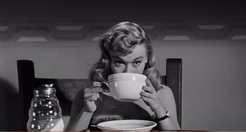 Movie still from “The Incredible Shrinking Man” (1957), directed by Jack Arnold – A black and white photo of a woman drinking from a cup; Medium shot, Low angle