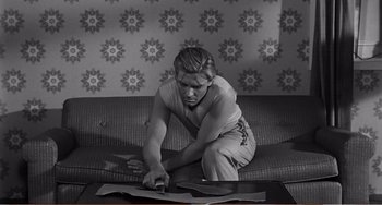 Movie still from “The Incredible Shrinking Man” (1957), directed by Jack Arnold – A woman sitting on a couch looking at papers on a table; Medium shot, High angle