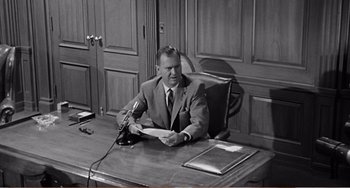 Movie still from “The Incredible Shrinking Man” (1957), directed by Jack Arnold – A man sitting at a desk in front of a microphone; Medium shot, Low angle