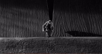Movie still from “The Incredible Shrinking Man” (1957), directed by Jack Arnold – A man standing on top of a tree trunk; Wide shot, High angle