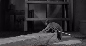 Movie still from “The Incredible Shrinking Man” (1957), directed by Jack Arnold – A man is bending over a piece of wood; Wide shot, High angle