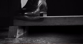 Movie still from “The Incredible Shrinking Man” (1957), directed by Jack Arnold – A pair of black shoes sitting on top of a wooden shelf; Extreme Close Up shot, Low angle