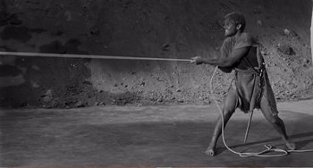 Movie still from “The Incredible Shrinking Man” (1957), directed by Jack Arnold – A man holding onto a long wooden stick while standing on a cement floor; Wide shot, High angle
