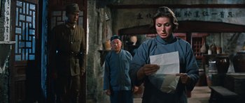 Movie still from “The Inn of the Sixth Happiness” (1958), directed by Mark Robson – A woman is holding a piece of paper while standing next to two men; Medium shot, Low angle