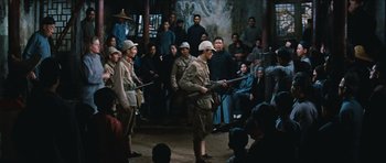 Movie still from “The Inn of the Sixth Happiness” (1958), directed by Mark Robson – A group of men standing in front of an audience holding guns; Wide shot, Over the shoulder angle