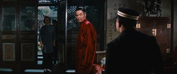 Movie still from “The Inn of the Sixth Happiness” (1958), directed by Mark Robson – A man in a red shirt is standing in front of another man in a black hat; Medium shot, Over the shoulder angle