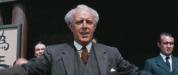 Movie still from “The Inn of the Sixth Happiness” (1958), directed by Mark Robson – An older man in a gray suit and a brown tie; Close Up shot, Low angle