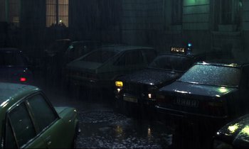 Movie still from “The Grilling” (1981), directed by Claude Miller – A bunch of cars are parked in a parking lot in the rain; Wide shot, High angle
