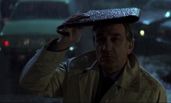 Movie still from “The Grilling” (1981), directed by Claude Miller – A man in a raincoat and tie holding a piece of paper; Close Up shot, Low angle