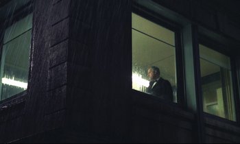 Movie still from “The Grilling” (1981), directed by Claude Miller – A man in a suit looking out of a window at night; Wide shot, Low angle
