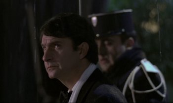 Movie still from “The Grilling” (1981), directed by Claude Miller – A man in a suit and tie next to another man in a uniform; Close Up shot, Low angle