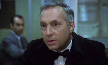 Movie still from “The Grilling” (1981), directed by Claude Miller – An older man in a black suit and a bow tie; Close Up shot, Over the shoulder angle