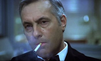 Movie still from “The Grilling” (1981), directed by Claude Miller – A person wearing a suit smoking a cigarette; Close Up shot, Low angle