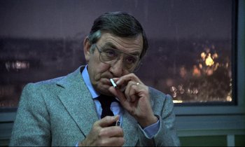 Movie still from “The Grilling” (1981), directed by Claude Miller – An older man smoking a cigarette in front of a window; Close Up shot, Low angle
